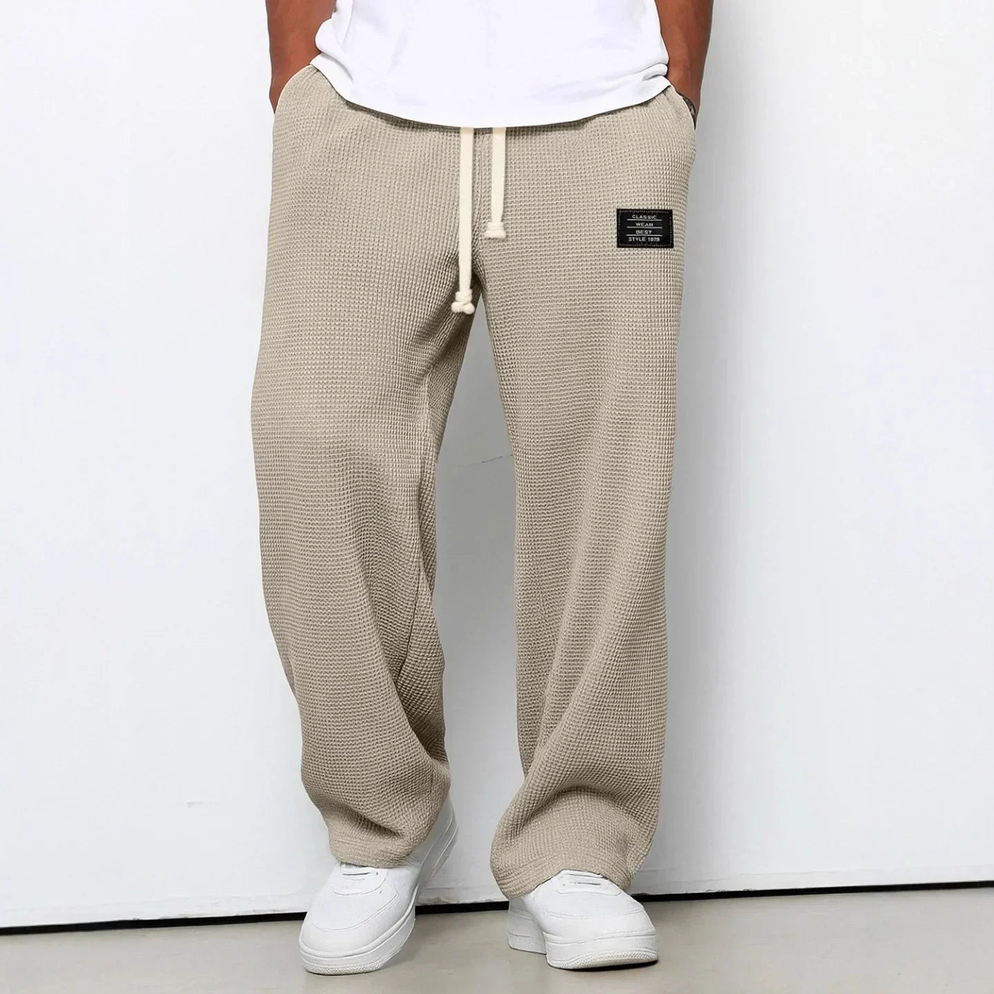 Beige waffle-knit relaxed fit jogger pants with drawstring waist and patch detail, streetwear style.