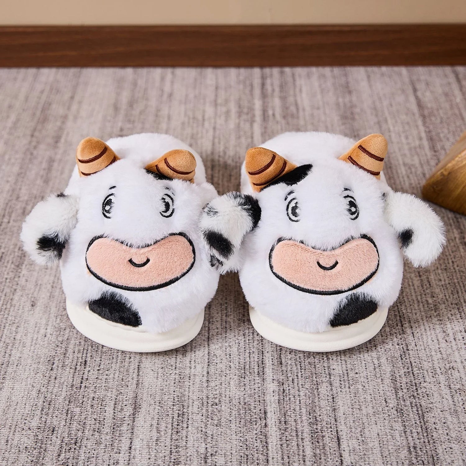 Cute plush cow slippers, white and black, soft material, cozy fit, on carpeted floor