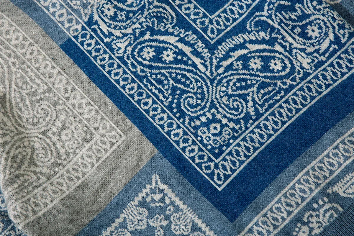 Close-up of blue and grey knit sweater fabric with paisley and geometric patterns.