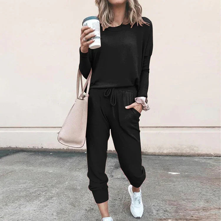 Woman wearing black casual jogger set with long sleeves, tapered pants, and white sneakers