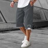 Man wearing loose-fit dark gray streetwear shorts with white trim and drawstring, outdoor setting