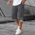 Man wearing loose-fit dark gray streetwear shorts with white trim and drawstring, outdoor setting