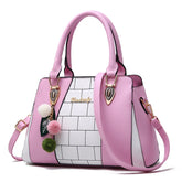 Pastel pink and white structured handbag with colorblock pattern, gold hardware, and pom pom charm.