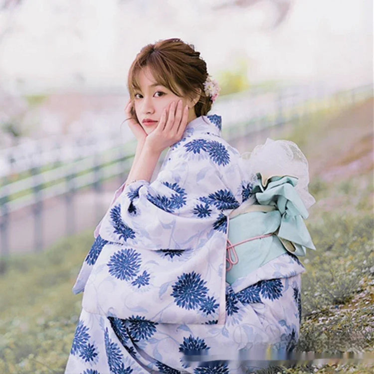 Woman wearing light blue floral kimono with wide sleeves and decorative sash, sitting outdoors