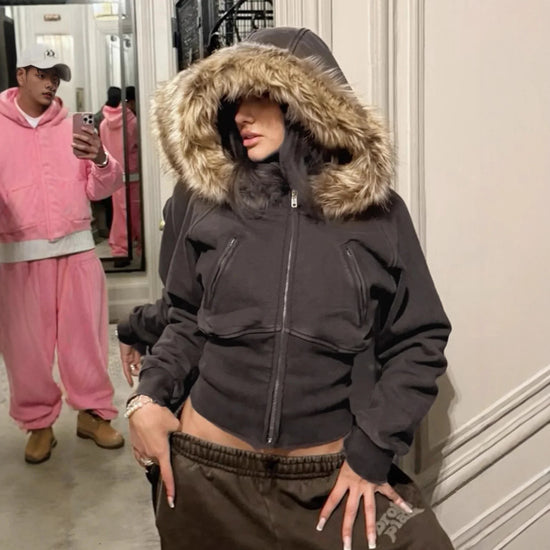 Woman in a fitted black hoodie with faux fur trim and brown sweatpants, streetwear style.