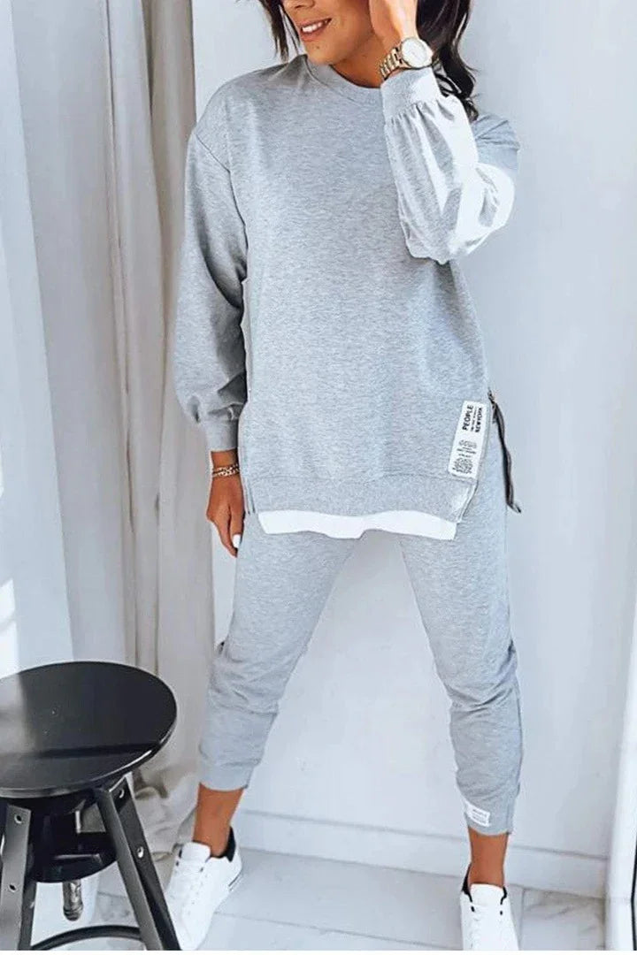 Woman wearing light gray oversized sweatshirt and jogger pants set, cotton material, relaxed fit streetwear.