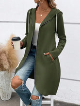 Woman wearing long olive green zip-up hoodie with pockets, white tank top, ripped blue jeans