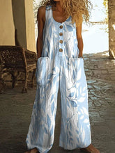 Woman wearing loose fit sleeveless jumpsuit with blue and white leaf print, large front pockets, and button front detailing.