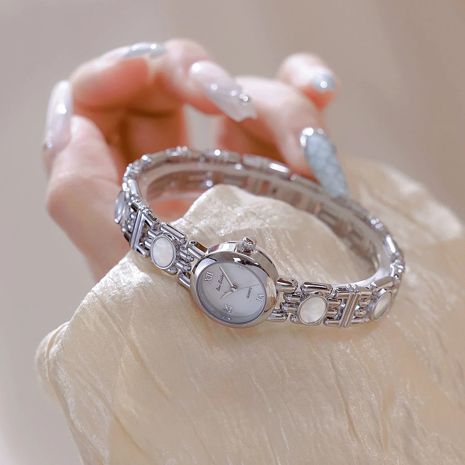 Elegant silver bracelet watch with white face and round accents, worn with silky beige sleeve.