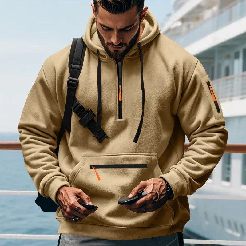 Man wearing a beige oversized streetwear hoodie with black drawstrings and multiple zip pockets
