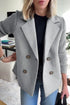 Woman wearing a light gray double-breasted blazer with ribbed knit sleeves, casual fit, paired with jeans.