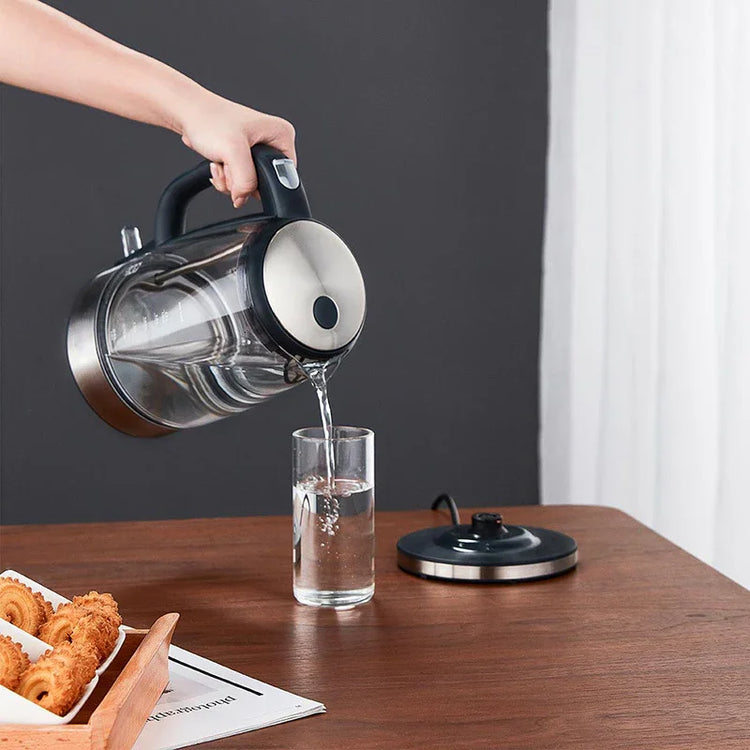 Hand pouring water from a transparent electric glass kettle into a clear glass
