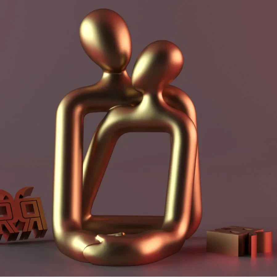 Abstract gold metallic sculpture of two faceless figures embracing on a smooth surface
