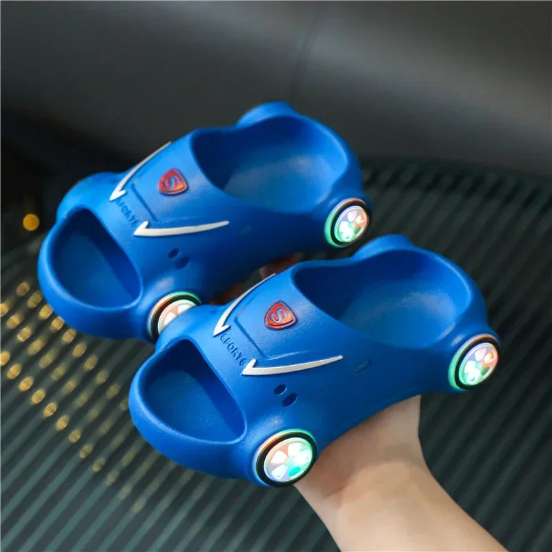 Blue car-shaped slip-on sandals with open toe, light-up wheels, and molded rubber style.