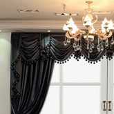 Black velvet draped curtain with pom pom trim in a modern living room setting