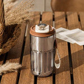Stainless steel insulated tumbler with brown lid and digital temperature display, on a wooden table.