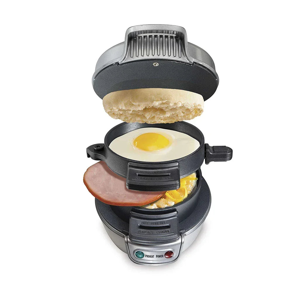 Breakfast sandwich maker with layers of egg, ham, cheese, and English muffin being assembled.