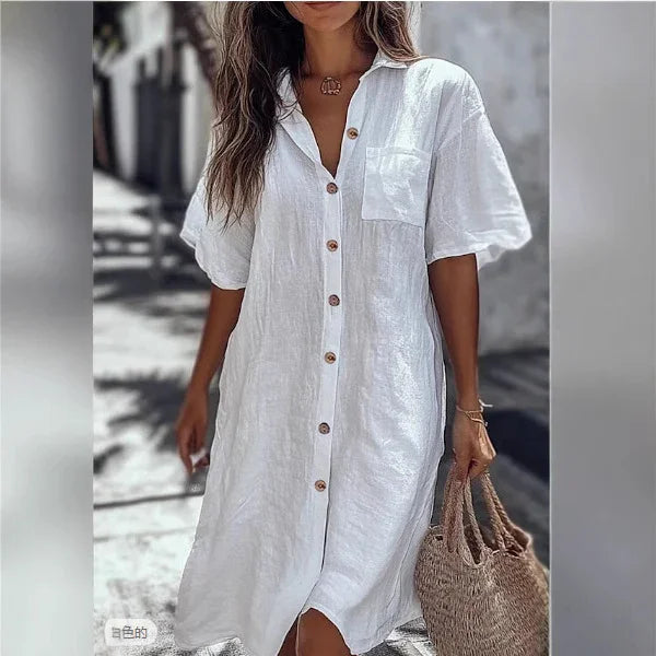 Woman wearing loose white linen button-up shirt dress with short sleeves, front pocket, and relaxed fit