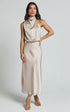 Woman wearing a sleeveless champagne satin midi dress with draped high neckline and slim fit