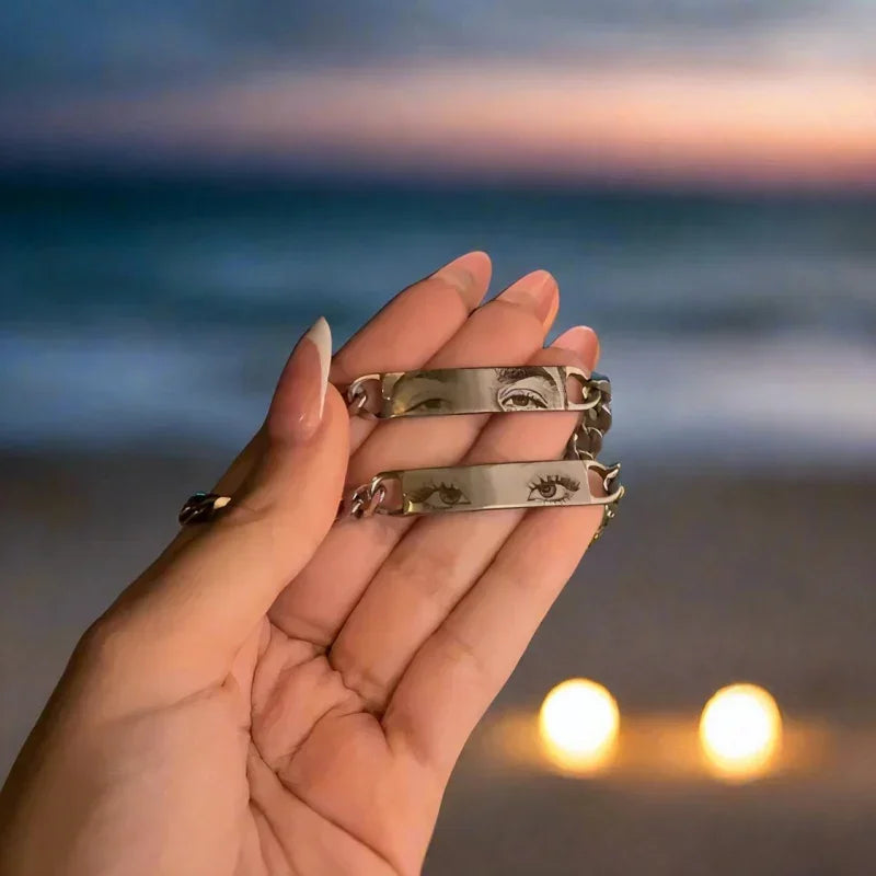 Hand holding silver engraved eye bracelets with chain links, beach sunset background