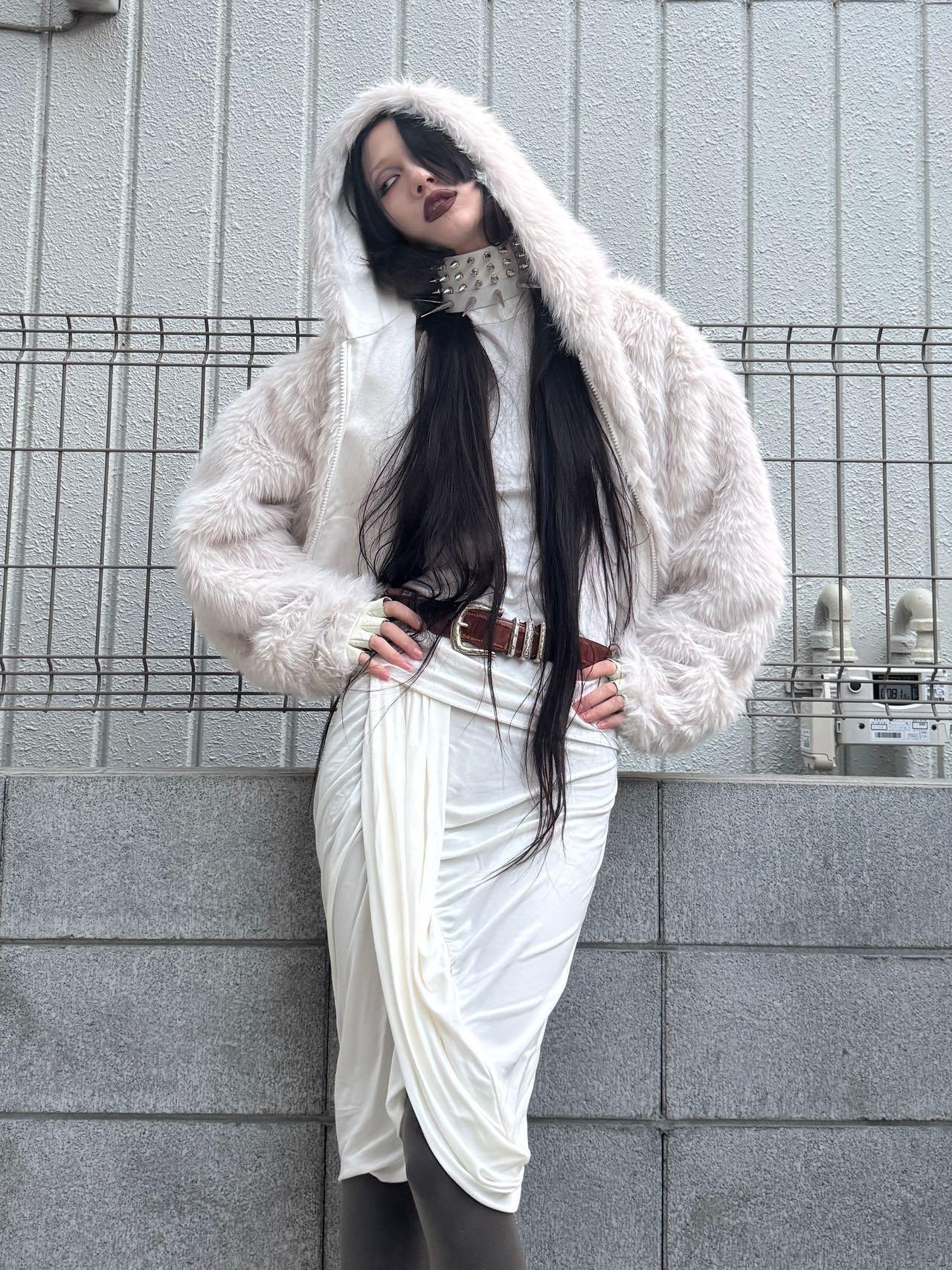Woman wearing oversized faux fur white hooded jacket, draped white skirt, and studded choker