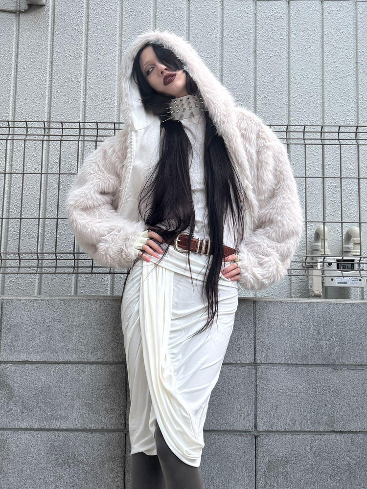 Woman wearing oversized faux fur white hooded jacket, draped white skirt, and studded choker