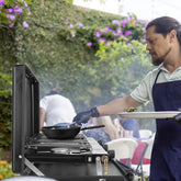 Man in a short sleeve polo and navy apron grilling outdoors, wearing black gloves