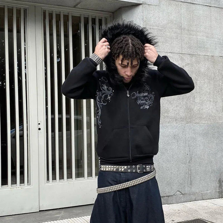 Man wearing a black zip-up hoodie with faux fur hood, gothic print, and baggy jeans with studded belts
