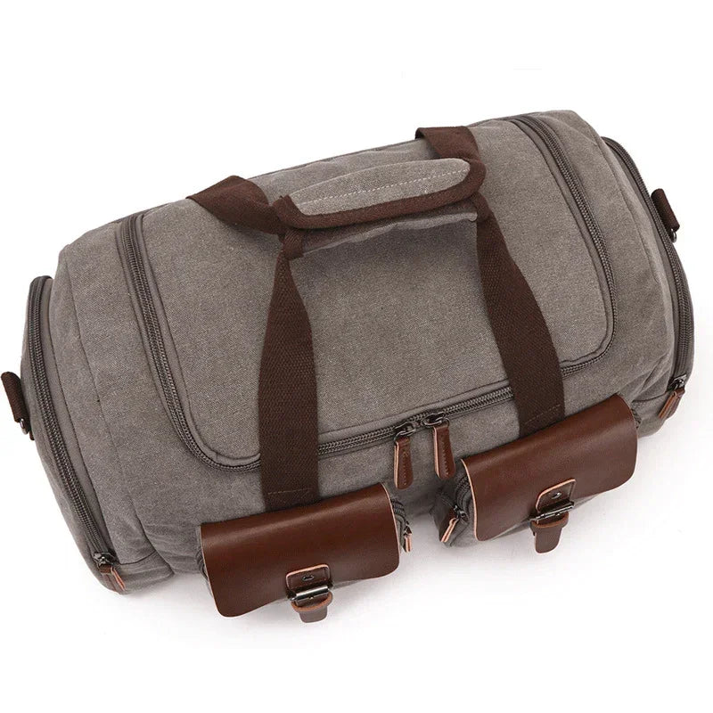 Gray canvas duffel bag with brown leather accents and multiple zippered pockets