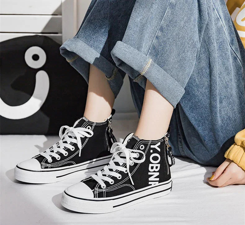 Black canvas high-top sneakers with white laces and bold lettering, paired with wide-leg cuffed denim jeans.