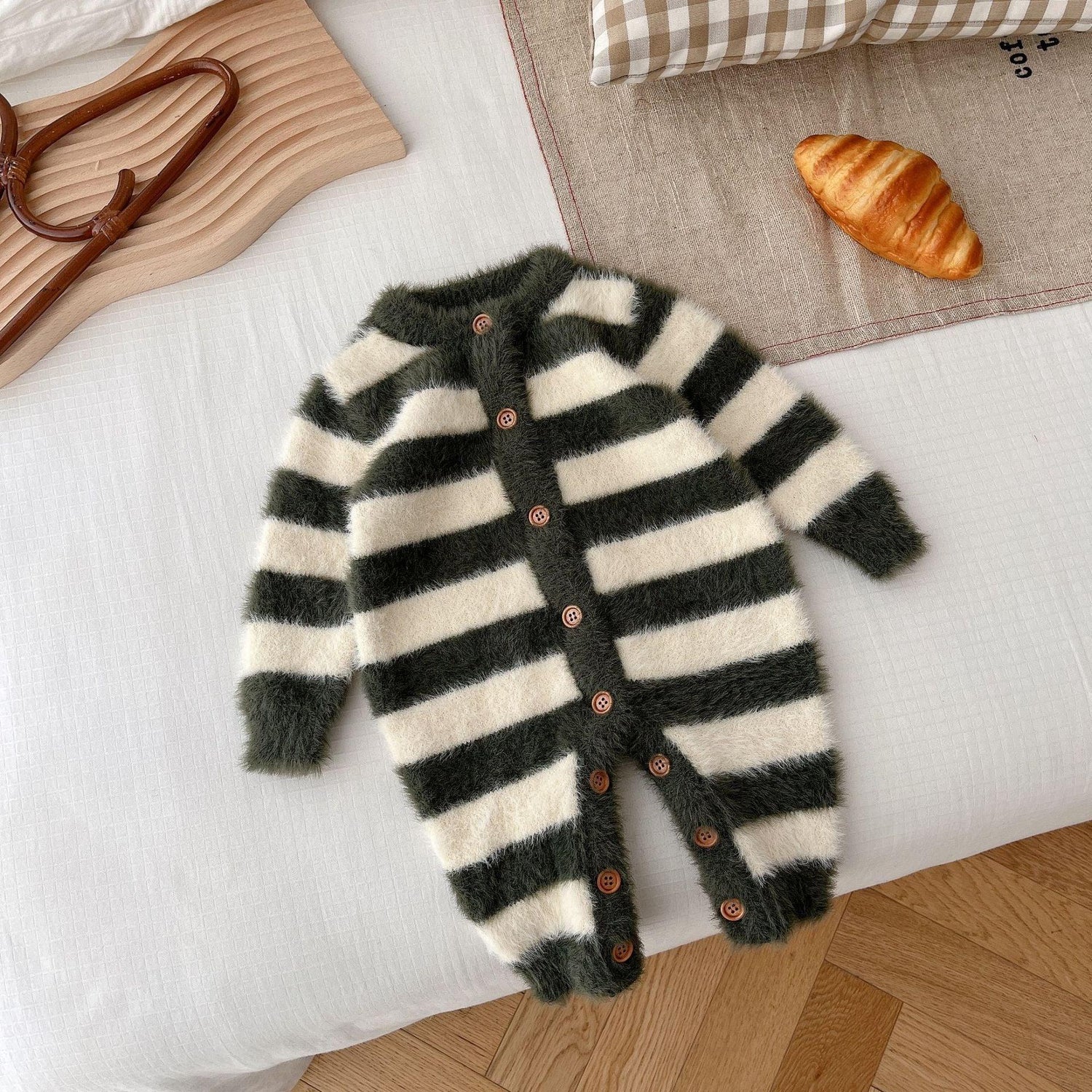 Fuzzy black and white striped baby jumpsuit with wooden buttons, laid flat on a bed