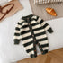 Fuzzy black and white striped baby jumpsuit with wooden buttons, laid flat on a bed