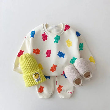 Kids' cream sweatshirt and pants with colorful bear prints, yellow knit beanie, fuzzy slippers
