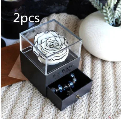 White preserved rose in clear acrylic box with drawer displaying dark beaded bracelet