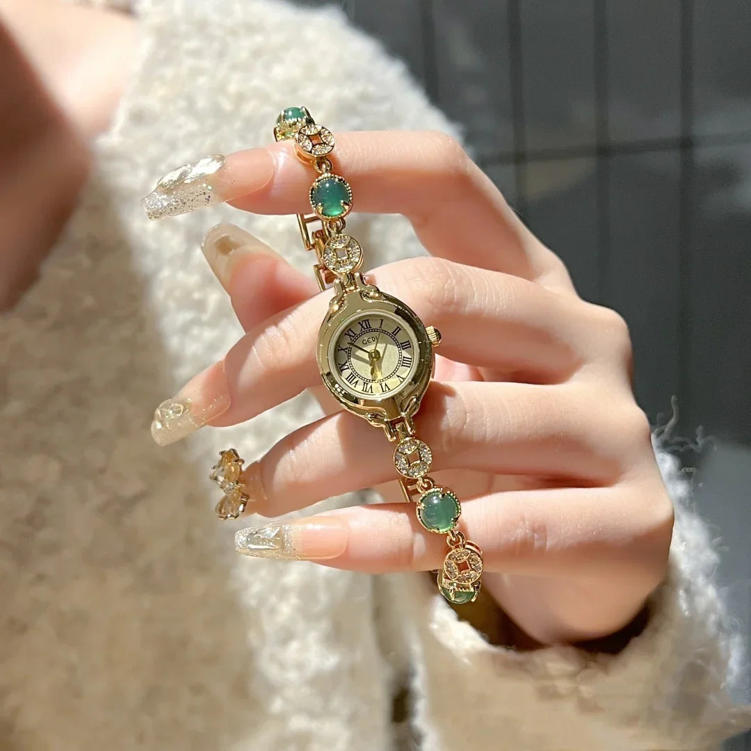 Gold bracelet watch with gemstone accents, worn with a textured cream sweater