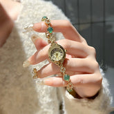 Gold bracelet watch with gemstone accents, worn with a textured cream sweater