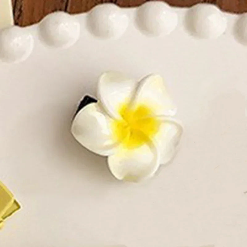 White and yellow plumeria flower hair clip with realistic petals on a decorative tray