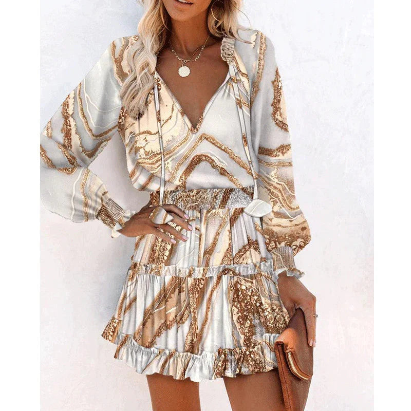 Woman wearing long sleeve marble print mini dress with ruffled hem and relaxed fit, beige and gold tones.