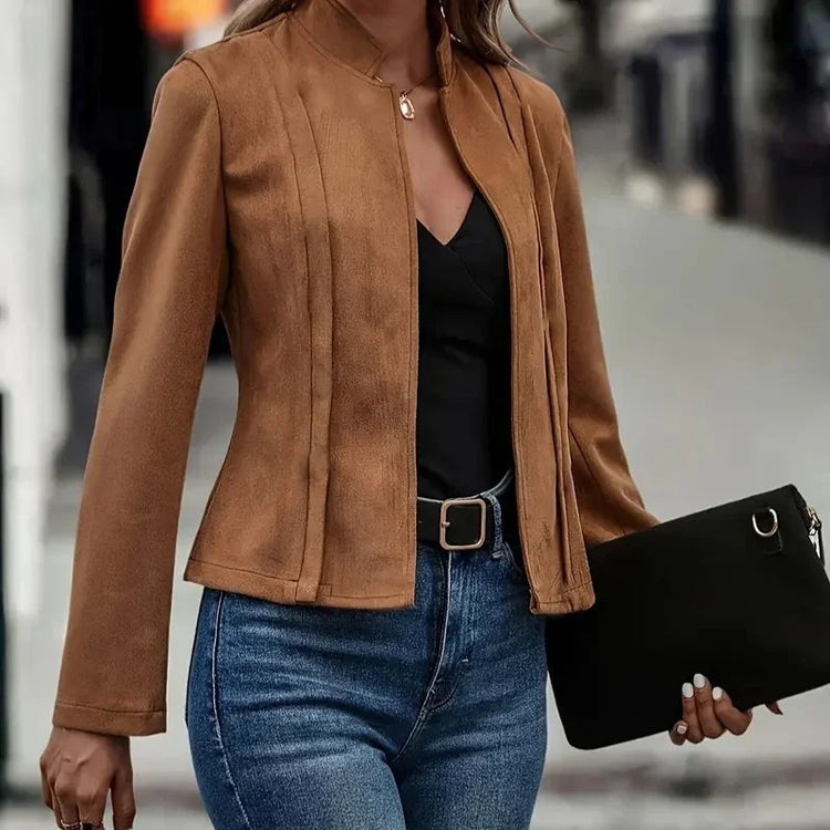 Woman wearing a fitted brown suede jacket, black top, and blue high-waisted jeans on street.