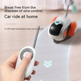 Hand holding wireless remote control for toy car with orange wheels on wooden floor