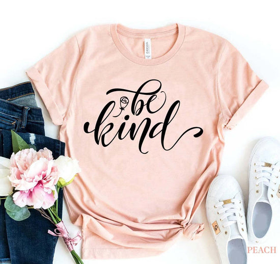 Peach Be Kind T-shirt with black script text, soft cotton fabric, paired with jeans, white sneakers, and flowers.