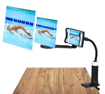 Adjustable black phone holder with flexible arm and clamp on wood table, holding smartphone horizontally