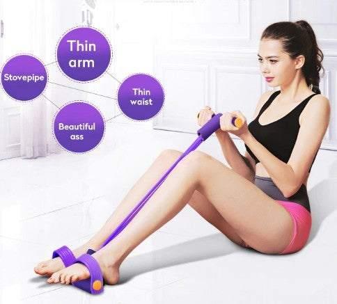Woman wearing black crop top and pink shorts, sitting indoors, using purple resistance band for exercise.