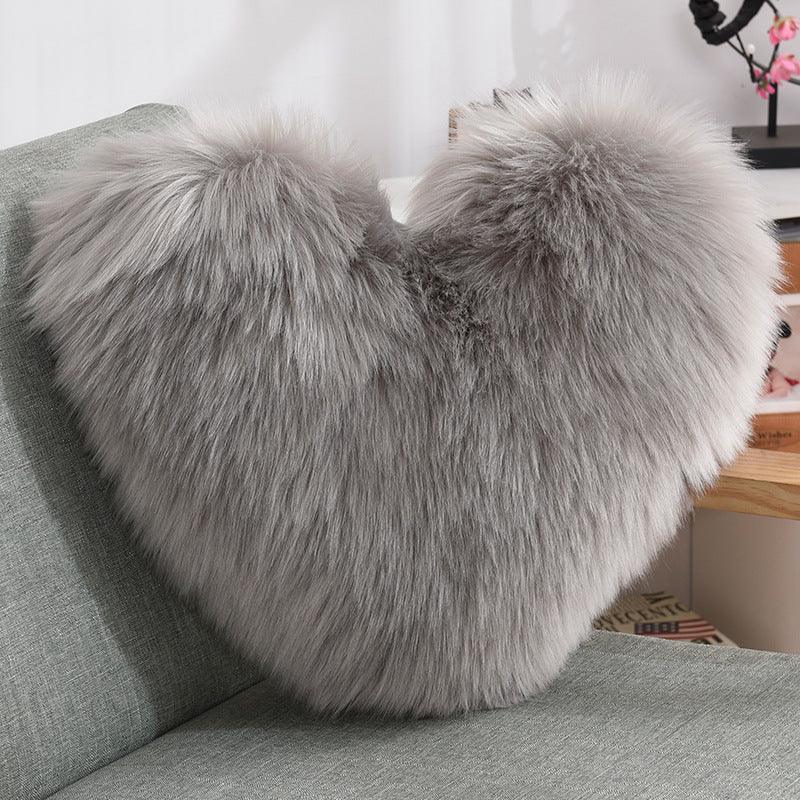 Plush heart-shaped throw pillow in grey faux fur with soft, fluffy texture on a sofa
