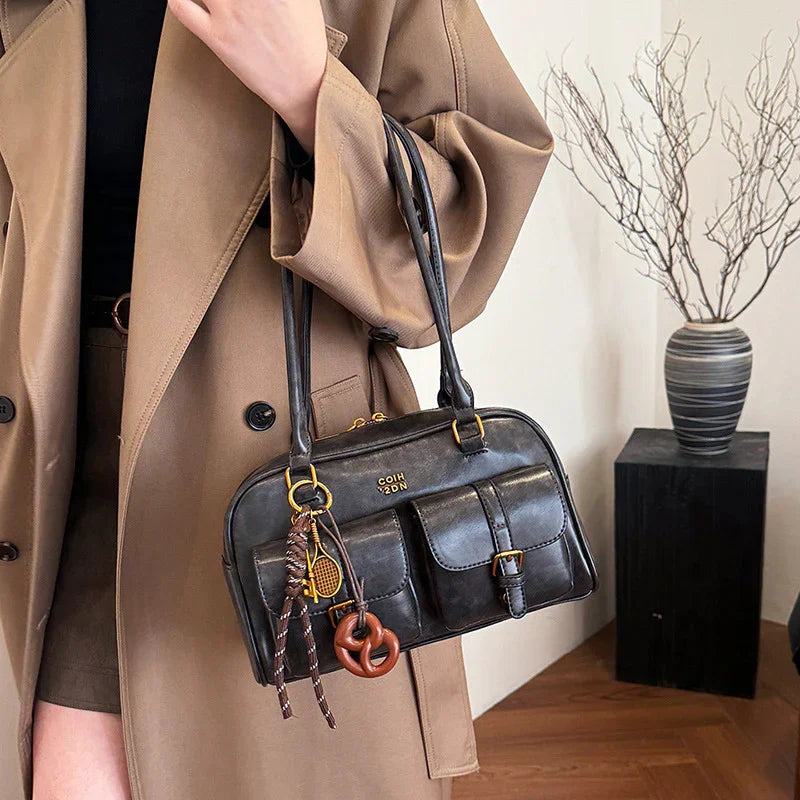 Woman wearing an oversized tan trench coat with a black leather shoulder bag and front pockets.