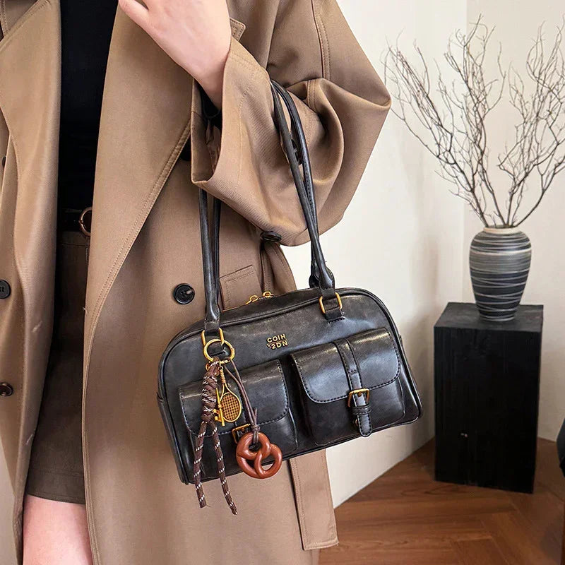 Woman wearing an oversized tan trench coat with a black leather shoulder bag and front pockets.