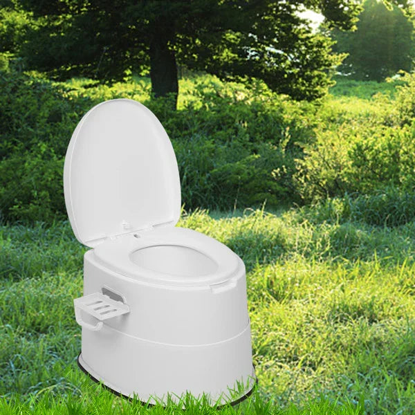 Portable white plastic toilet with lid open on grassy outdoor landscape