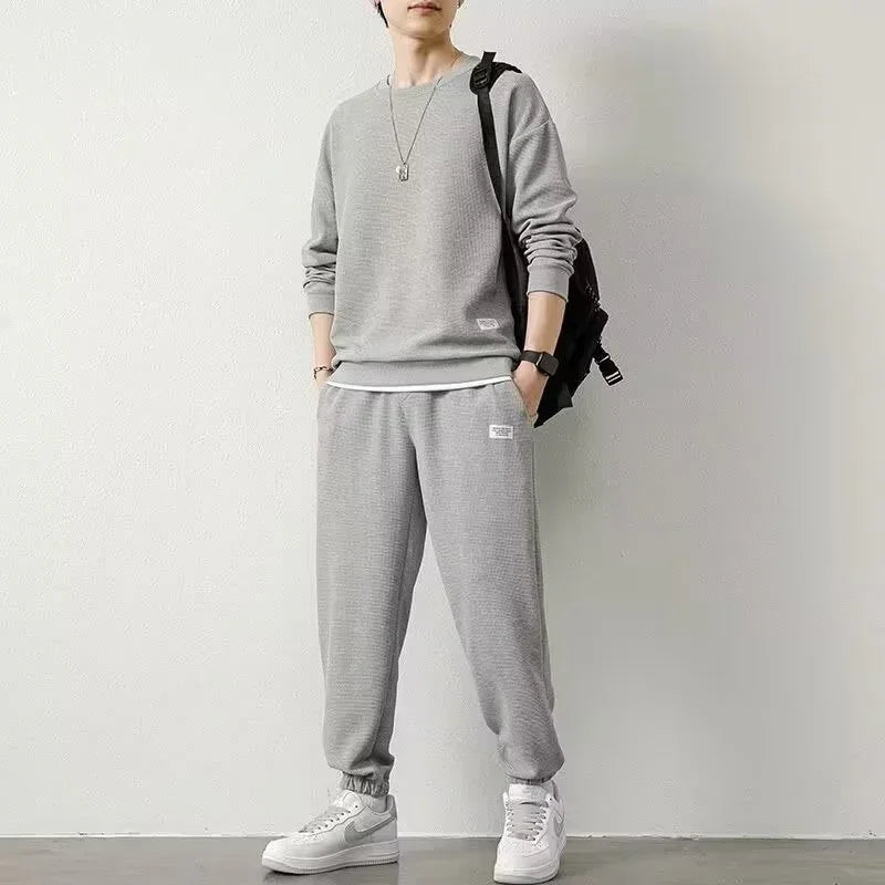 Man wearing light gray crewneck sweatshirt and jogger pants set, relaxed fit, cotton material, casual streetwear style.