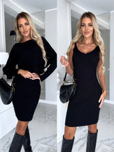 Woman modeling black ribbed knit mini dress, fitted silhouette, long sleeves and sleeveless options, paired with knee-high boots and a black shoulder bag, in a modern indoor setting.
