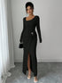 Woman wearing a long black ribbed bodycon dress with front slit, asymmetrical neckline, and metal ring detail, styled with clear heels and a small handbag.